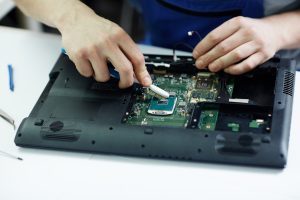 Closeup shot of male hands working on disassembling and cleaning circuit board in laptop using brush